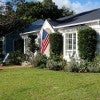 A small white house with lawn chairs out front and an American flag hanging