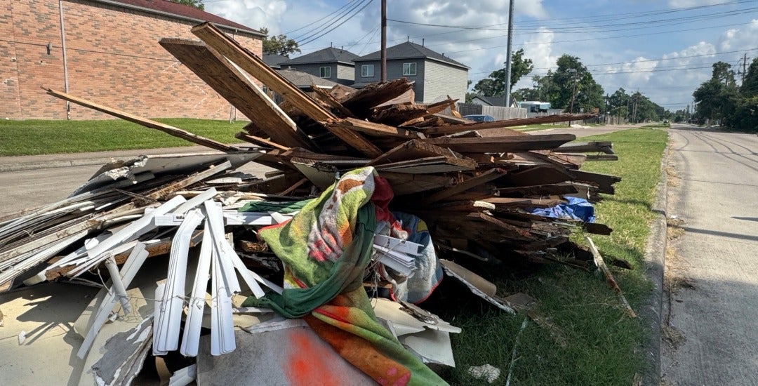 Piles of illegally dumped trash, including furniture, construction debris, and household waste, line a median in Houston.