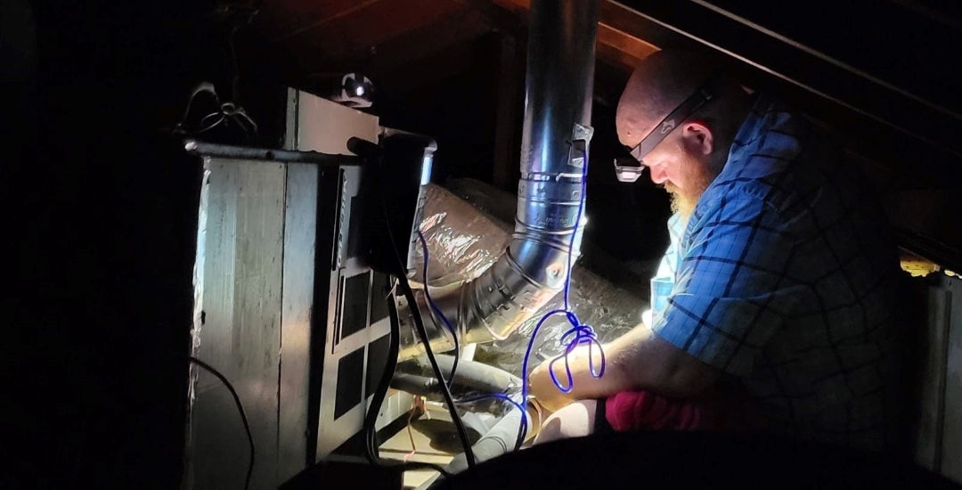BakerRipley quality assurance manager Jacob Smith tests the ventilation of a gas furnace in the flue.