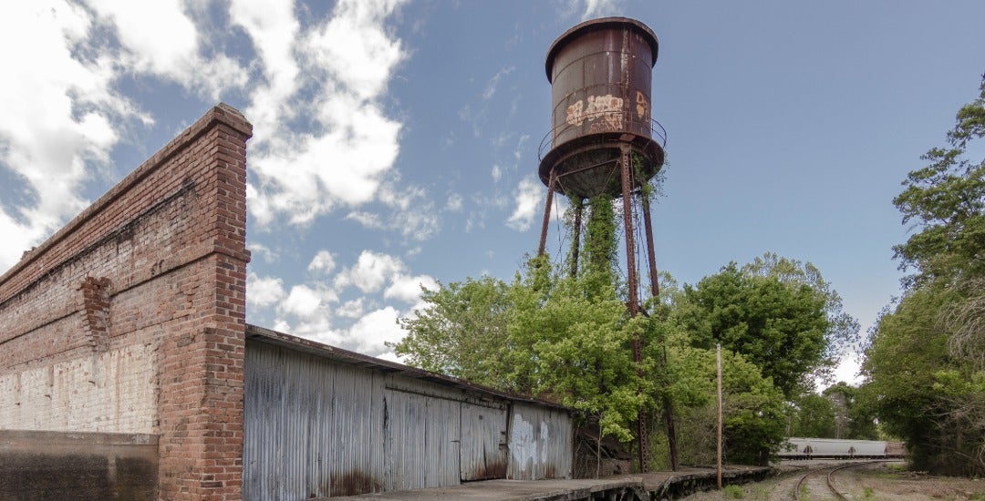 An abandoned factory and railroad near a large water tower.