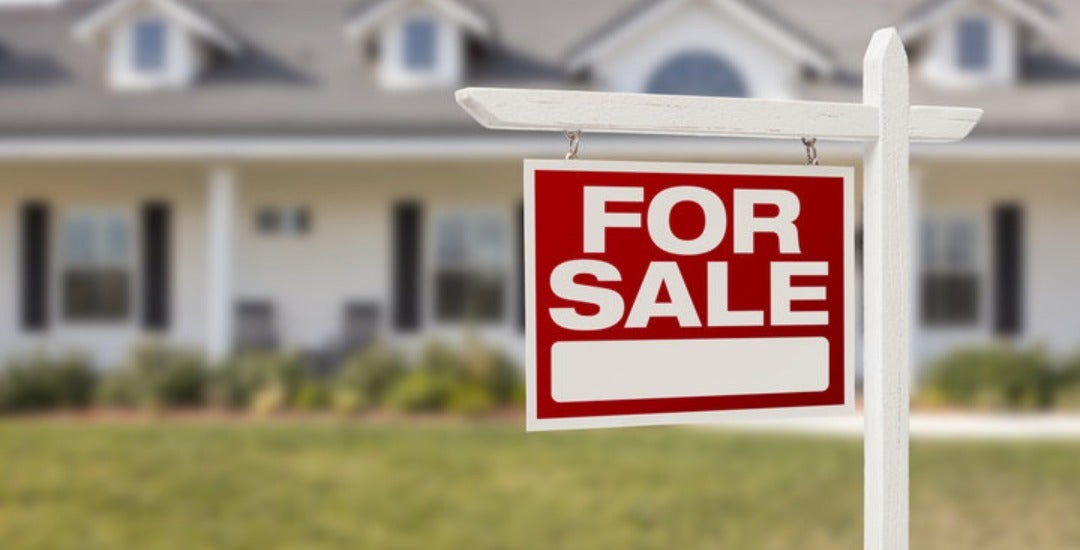 A single-story home with a "For sale" yard sign out front.