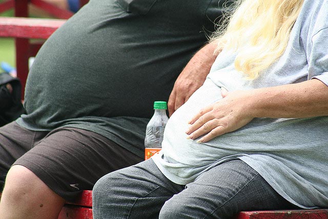 Two extremely overweight people sitting on a bench outside