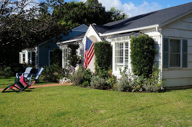 A small white house with lawn chairs out front and an American flag hanging