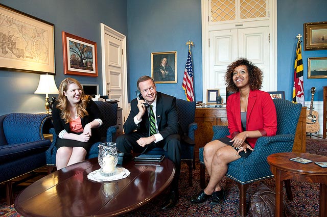 Martin O'Malley on the phone with two women sitting next to him