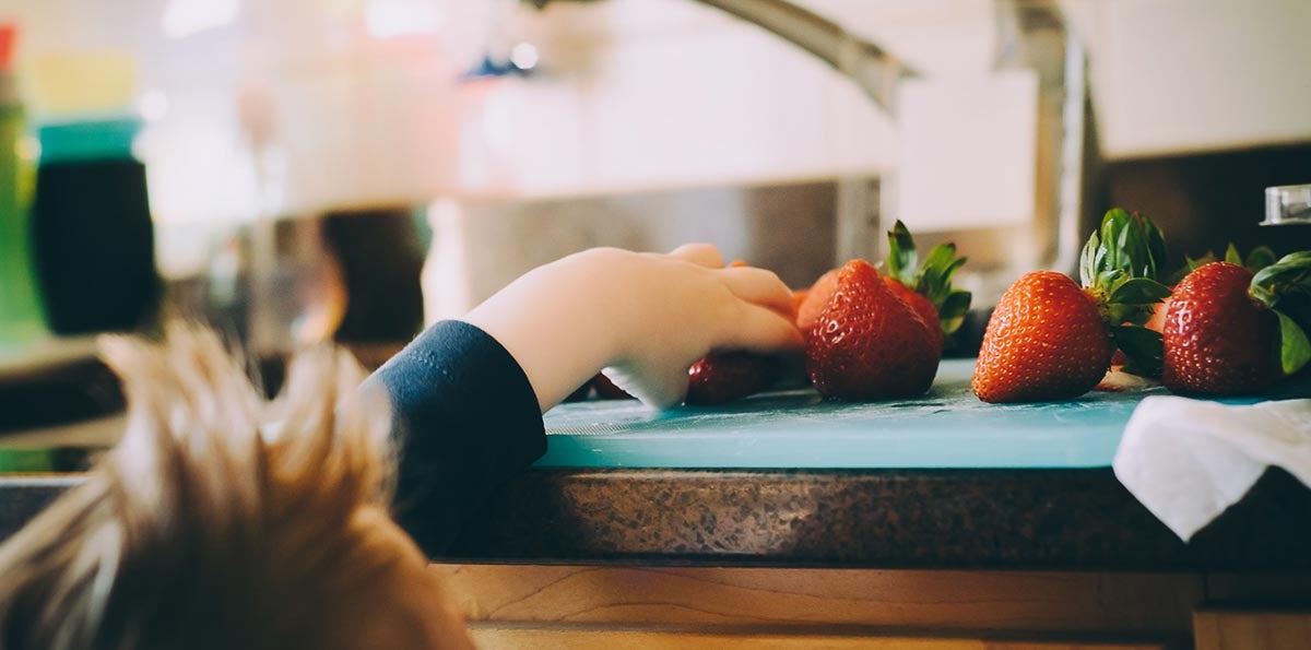 Child reaching for strawberries on counter