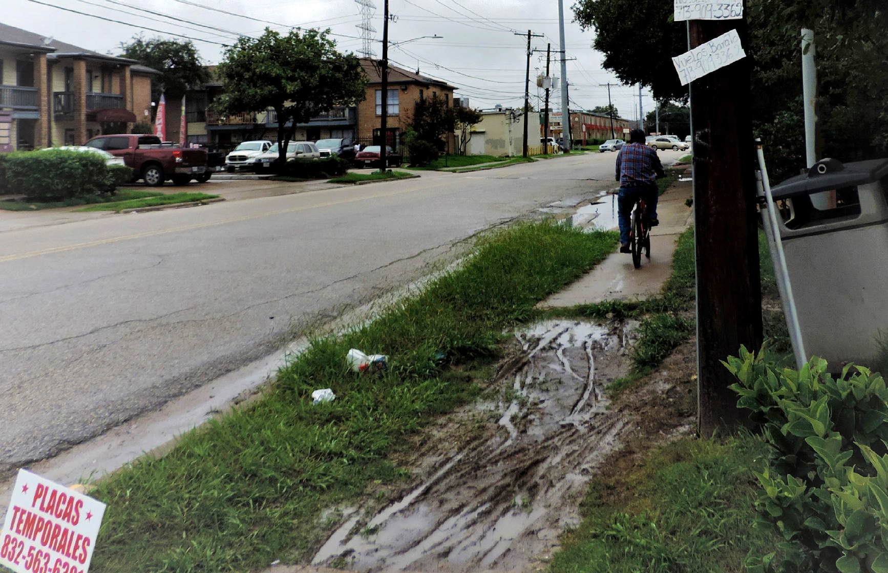 A muddy patch of grass interrupts the sidewalk in Gulfton as a bicyclist navigates onward