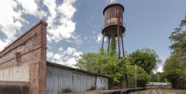 An abandoned factory and railroad near a large water tower.
