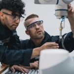Students work on a robotic arm in a technical workshop.