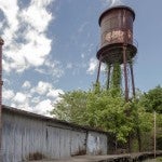 An abandoned factory and railroad near a large water tower.