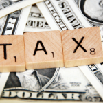 Scrabble letters spelling out "tax" over dollar bills