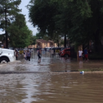 City truck moving through floodwaters where people are walking
