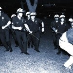 LAPD officers confront a protestor on the south lawn of City Hall while a police car burns during night one of the Rodney King Riots on April 29, 1992, in Los Angeles, California..