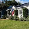 A small white house with lawn chairs out front and an American flag hanging A small white house with lawn chairs out front and an American flag hanging