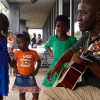 Man playing a guitar with children surrounding 