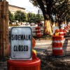 Sidewalk closed sign and traffic cones blocking sidewalk.