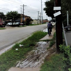 Man riding bike along rough, muddy sidewalk